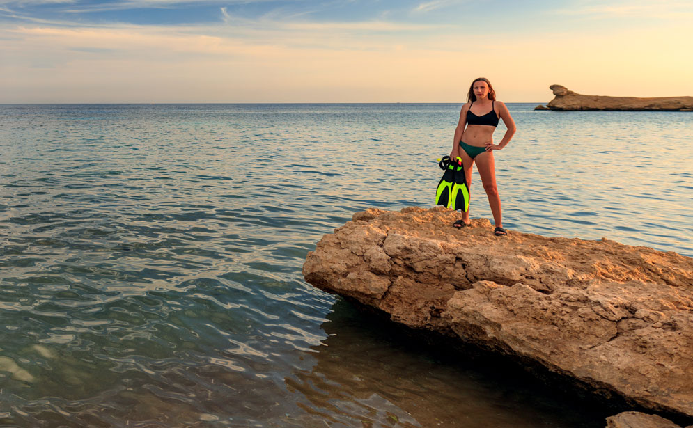 young-woman-standing-at-the-sea- shore diving - scuba diving - scubly